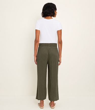Woman wearing a white t-shirt and green wide-leg pants on a plain background