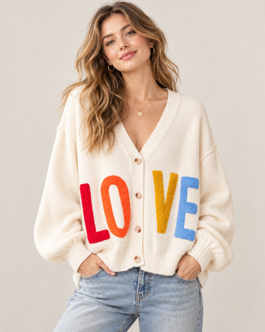 A woman wearing a beige v-neck cardigan with “LOVE” written in multi-colored letters at the middle of the sweater