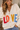 A woman wearing a beige v-neck cardigan with “LOVE” written in multi-colored letters at the middle of the sweater.