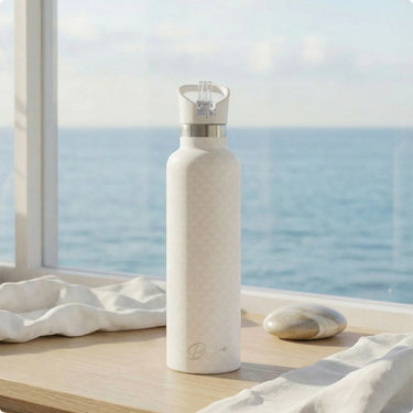 White water bottle with silver cap on a windowsill with a view of the ocean.