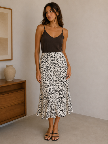 Woman wearing a black top and patterned skirt standing in a room with a wooden dresser and framed picture.