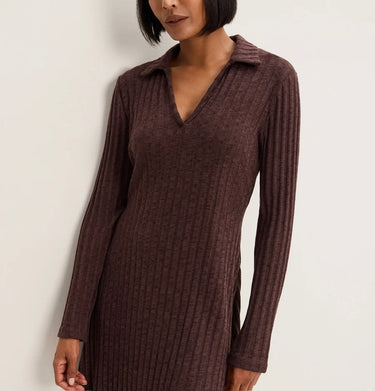 A woman wearing a ribbed knit long-sleeve polo dress in a dark brownish-purple color, shown from the neck down against a plain off-white background.
