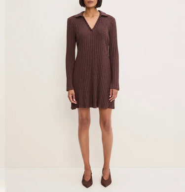 A woman modeling a ribbed knit long-sleeve mini dress in a dark brownish-purple color, paired with matching pointed-toe heels, against a plain off-white studio background.