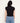 A woman viewed from the back wearing a fitted black sleeveless mock-neck top and light blue jeans against a plain off-white background.