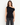 Delilah black drape top, front view showing asymmetrical off-the-shoulder neckline with dark jeans