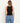 a woman wearing a black shine crop tank with ruched side detailing on a white background