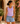 Woman wearing a purple tank top and denim shorts standing in front of a floral background