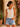 Woman wearing a white tank top and denim shorts standing in front of a floral wall.