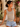 Woman wearing a gray tank top and denim shorts standing outdoors with plants in the background