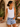 Woman wearing a white tank top and denim shorts standing outdoors.