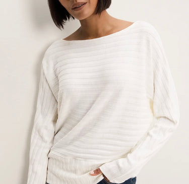 A woman wearing a white, long-sleeve knit sweater with a wide boat neckline and horizontal ribbed texture, shown against a plain off-white background.