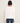 A woman viewed from the back wearing a cream-colored, long-sleeved ribbed knit top and dark blue jeans, set against a plain off-white background.