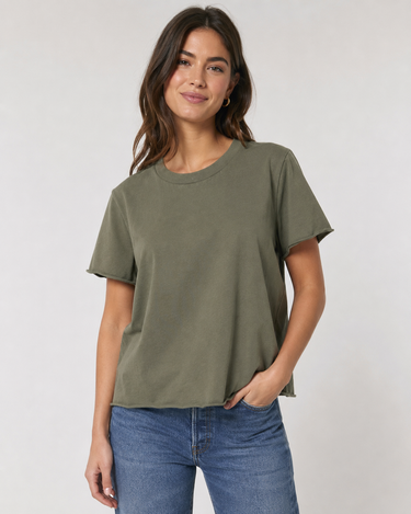 A woman wearing a relaxed-fit, short-sleeve crewneck t-shirt in olive green, paired with blue jeans, standing against a light gray studio background.