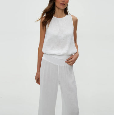 Woman wearing a white sleeveless top and pants on a plain background