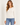 A woman wearing a chalk long sleeve crew tee and blue jeans on a white background.