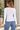 a woman wearing a white crew neck long sleeve and blue jeans in an outside setting.