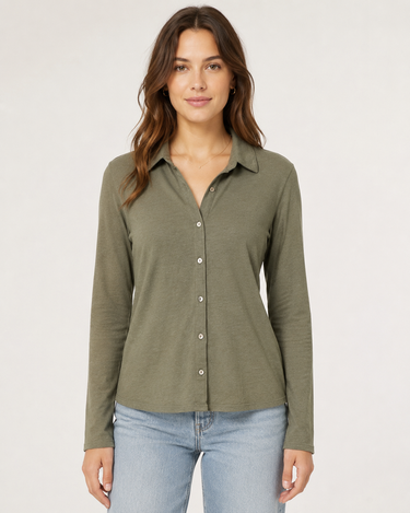 A woman modeling a long-sleeve button-up shirt in olive green, paired with light-wash blue jeans, against a plain light gray studio background.