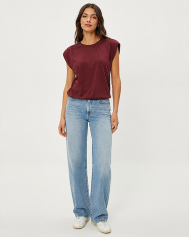 A woman modeling a sleeveless maroon top and light-wash blue jeans against a plain light gray studio background.