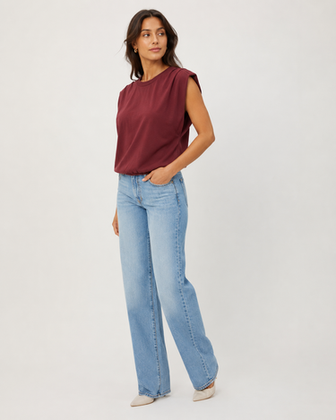 A woman modeling a sleeveless maroon top and light blue wide-leg jeans against a plain light gray studio background.