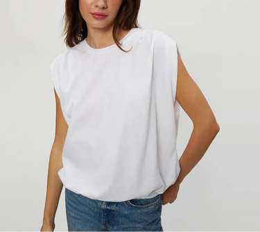 A woman wearing a white sleeveless top with a relaxed, draped fit and blue jeans, standing against a light gray studio background.