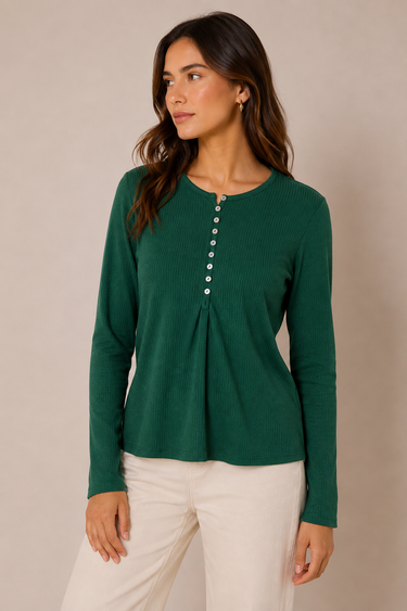 A woman wearing a dark green long-sleeve ribbed knit top with a buttoned neckline and cream pants, standing against a plain beige studio background.