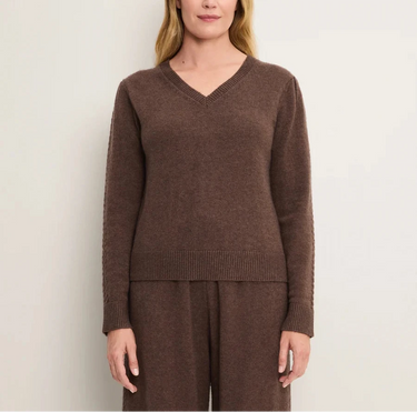 A woman wearing a knit v neck brown sweater and brown knit pants on a white background