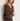 A woman wearing a knit v neck brown sweater and brown knit pants on a white background