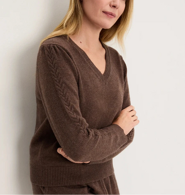 A woman wearing a knit v neck brown sweater and brown knit pants on a white background