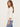 A woman wearing a white three-quarter sleeve t-shirt and blue jeans, shown from a side profile against a plain off-white studio background.