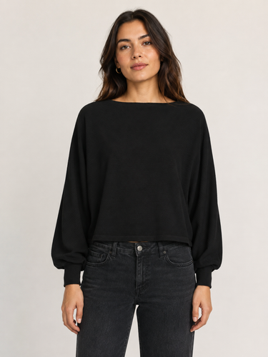 A woman modeling a black long-sleeve boat-neck top with balloon sleeves, paired with dark gray jeans, against a plain light gray studio background.
