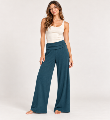 A woman wearing teal ribbed foldover pants, a white tank and sneakers on a white background.