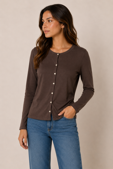 A woman wearing a dark brown long-sleeve button-front top and blue jeans, standing against a plain beige studio background.
