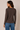 A woman shown from the back wearing a dark brown long-sleeve crewneck top and blue jeans, standing against a plain beige studio background.