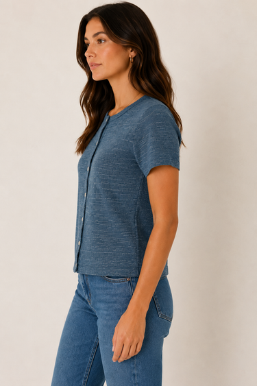 A woman wearing a short-sleeve textured blue top and blue jeans, shown in profile against a plain light beige studio background.
