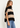 A woman wearing a beige and black stripe turtleneck poncho vest and blue jeans on a white background.