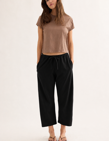 Woman wearing a brown crop top and black wide-leg pants on a white background