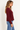 a woman wearing a burgundy ribbed v-neck cardigan and blue jeans on a white background.