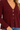 a woman wearing a burgundy ribbed v-neck cardigan and blue jeans on a white background.