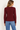 a woman wearing a burgundy ribbed v-neck cardigan and blue jeans on a white background.