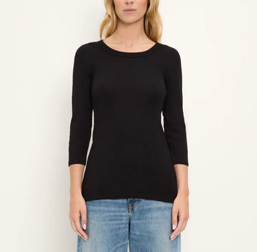 A woman wearing a black three-quarter sleeve crewneck top and blue jeans, standing against a plain off-white background.