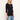 A woman wearing a black 3/4-sleeve crewneck knit top and light blue jeans, standing against a plain off-white studio background.