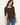 A woman wearing a brown ribbed 3/4-sleeve scoop-neck top and blue jeans, standing against a plain off-white background.