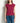A woman wearing a ribbed knit sleeveless top in deep burgundy and blue jeans, standing against a plain off-white wall.