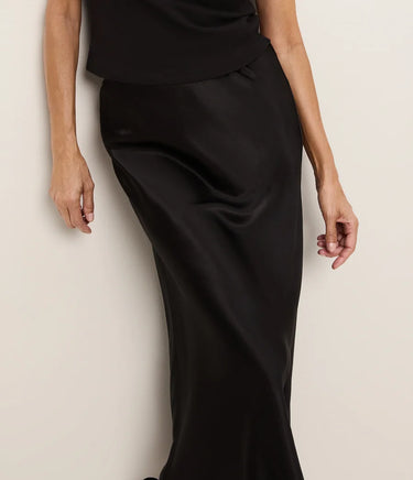 a woman wearing a black tee and a black bias midi skirt on a white background.