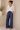 Woman wearing a white blouse and blue pants standing against a beige wall.
