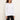 A woman wearing a plain white long-sleeve crewneck top and black pants, standing against a light beige studio background.