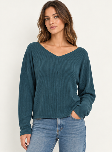 A woman wearing a teal ribbed long sleeve top and blue jeans on a white background.