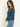 A woman wearing a teal ribbed long sleeve top and blue jeans on a white background.