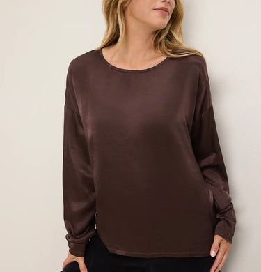 A woman wearing a dark brown long-sleeve top with a relaxed fit and a crew neckline, shown from the shoulders down against a plain light background.