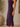 A woman wearing a sleeveless ruched midi dress in deep purple, standing indoors next to a large textured vase.